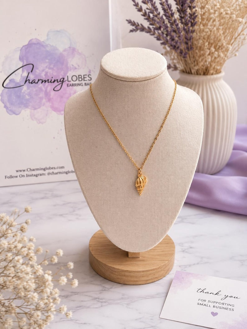 Gold conch shell necklace displayed on a bust stand